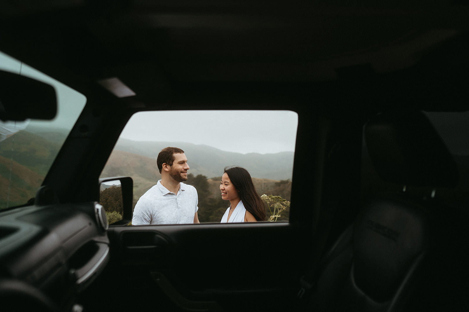 Picture shows a shoot through image of a jeep and a couple standing next to the window of the car.